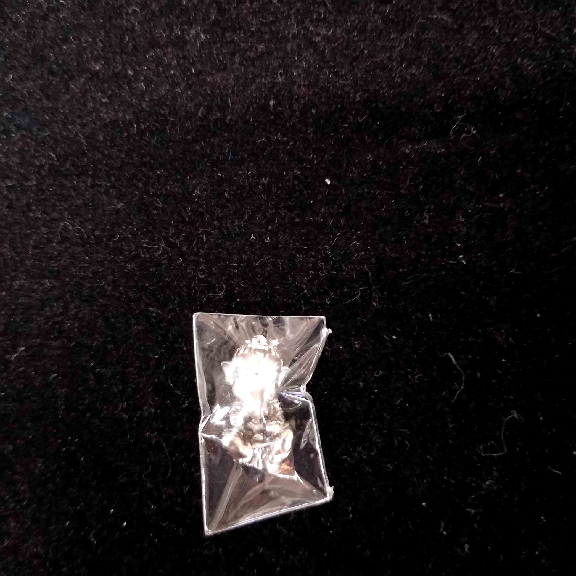 Sacred Thai Ganesh pendant silver amulet in clear plastic sleeve on black fabric background by Thai Blessing Co