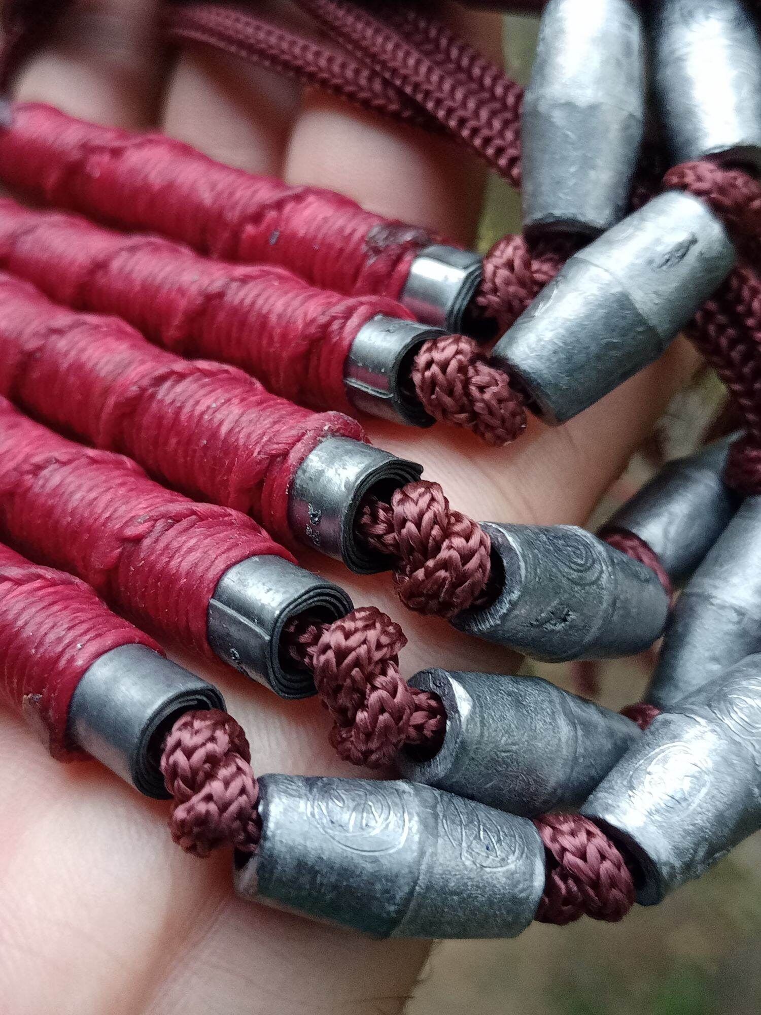 Closeup of multiple red braided cord amulets with metal scroll tubes Sacred Thai takrut blessed by Luang Pho Pleung