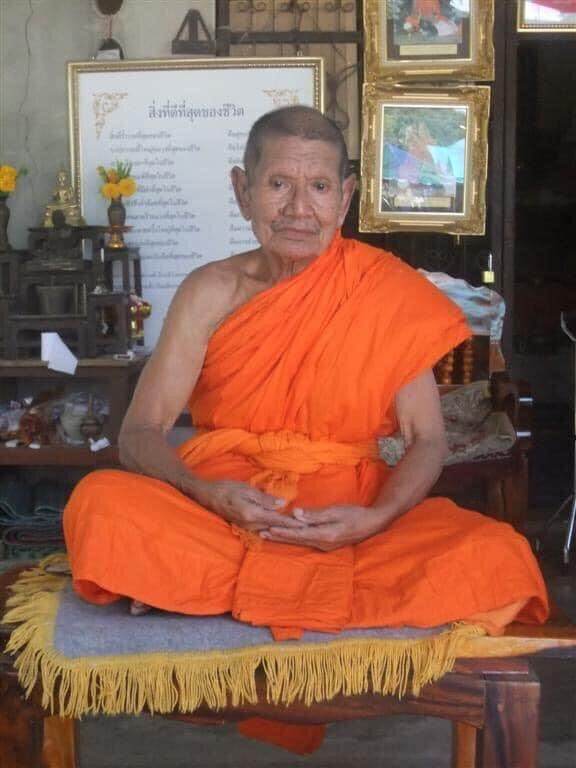 Sarika couple amulet for love presented by seated Buddhist monk in orange robes at shrine altar