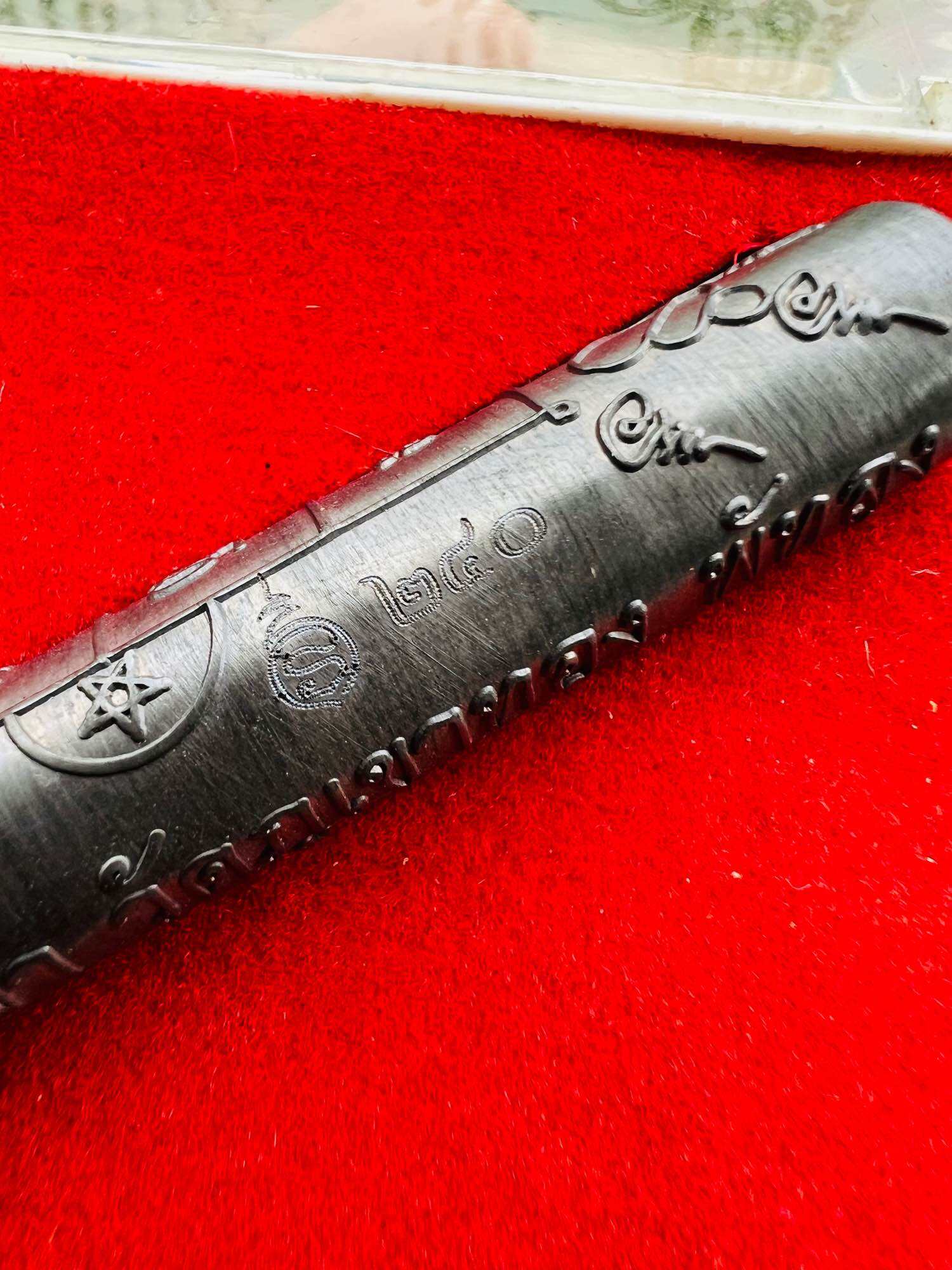 Takrut Jan Pen Full Moon Phayak Taksila black engraved amulet cylinder on red velvet background Thai Blessing Co
