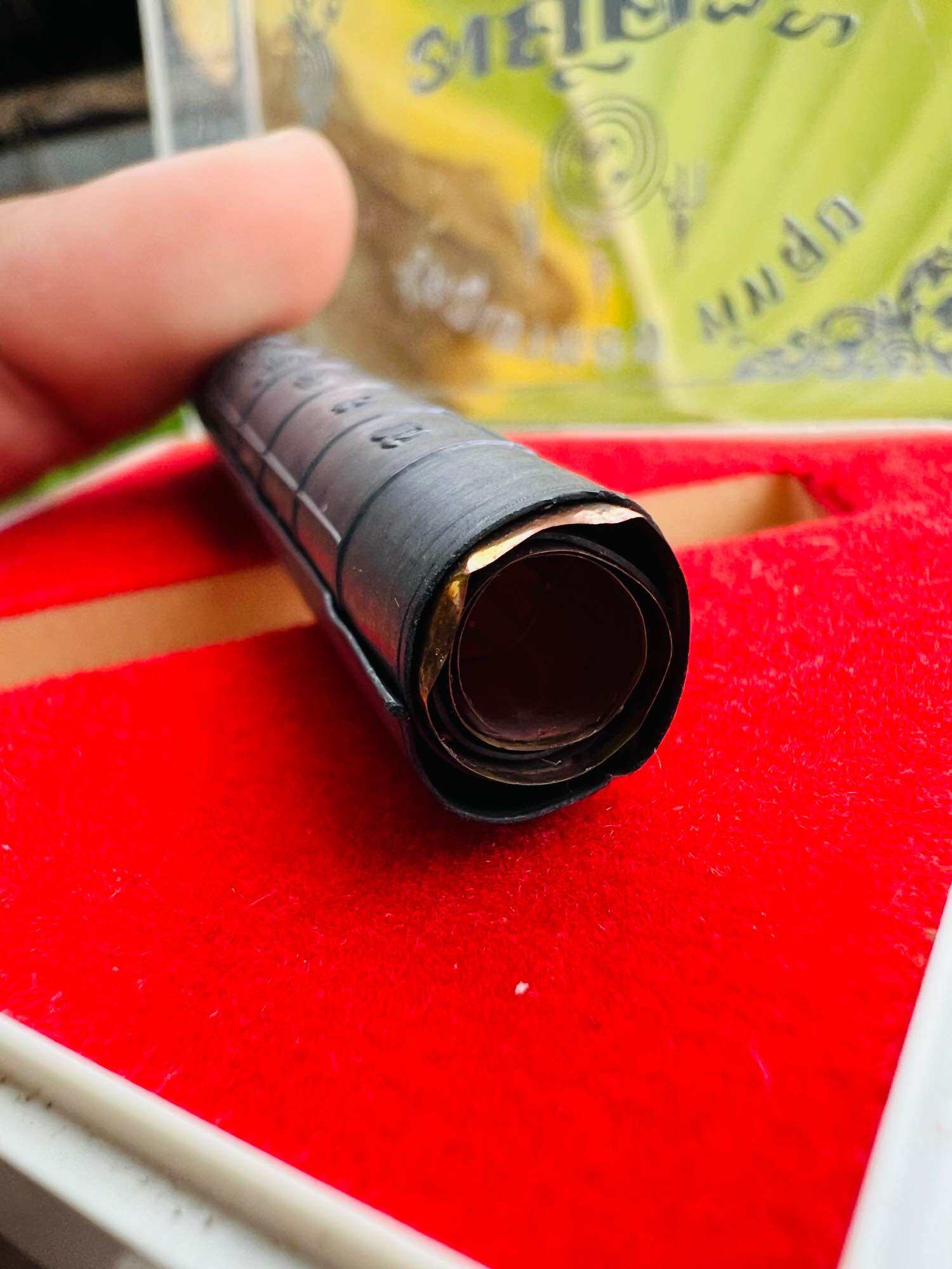 Takrut Jan Pen Full Moon Phayak Taksila black rolled amulet tube on red velvet display held by hand