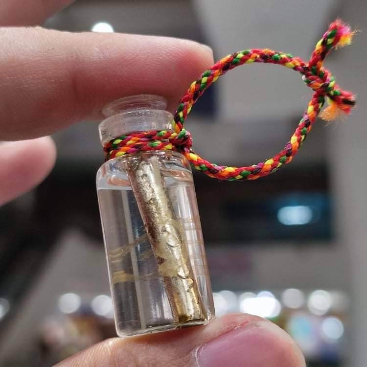 Small glass vial of Thai attraction oil for love with gold leaf charm and braided cord pendant