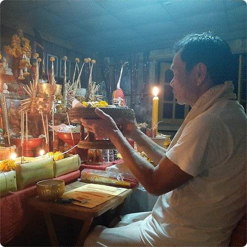 Man performing a candlelit altar ritual with offerings using Thai attraction oil for love by Thai Blessing Co