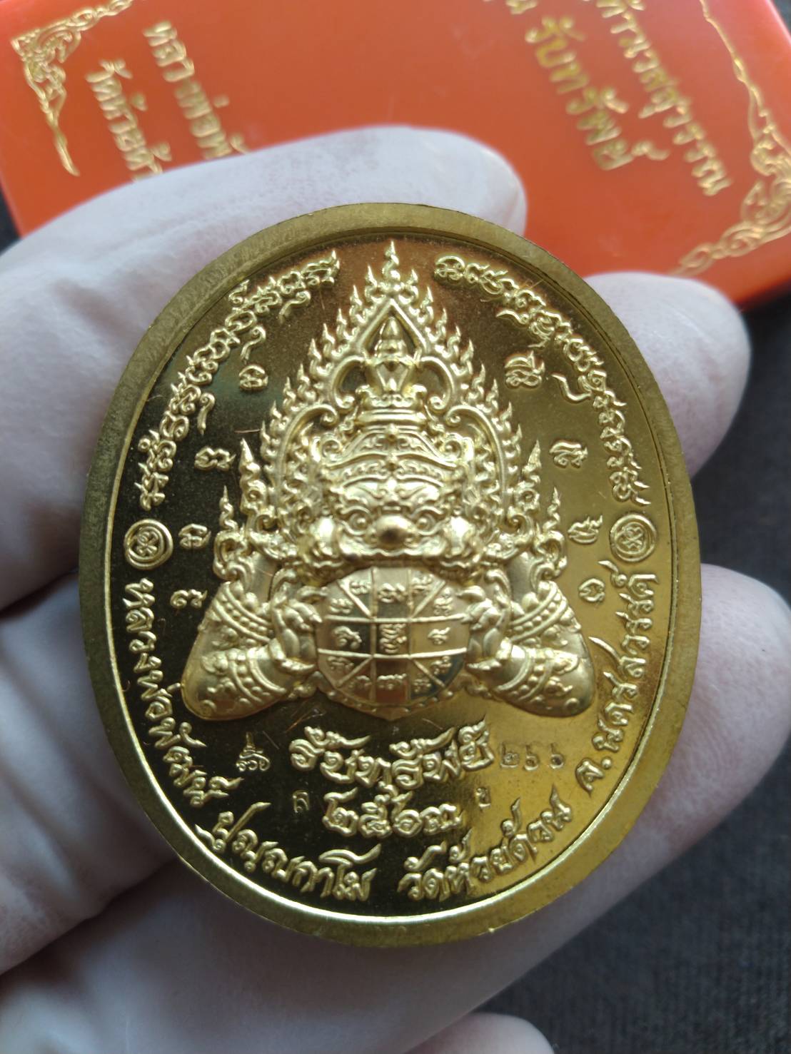 Gold oval Thao Wessuwan amulet blessed by Luang Pho Phat pendant held in gloved hand with red box