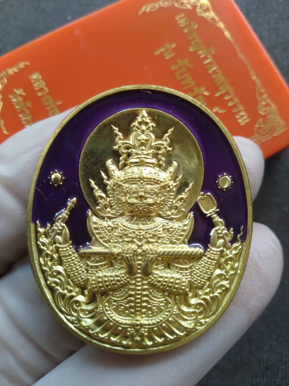 Thai Blessing Co Thao Wessuwan amulet blessed by Luang Pho Phat. Gold oval medallion with purple enamel detailed deity held