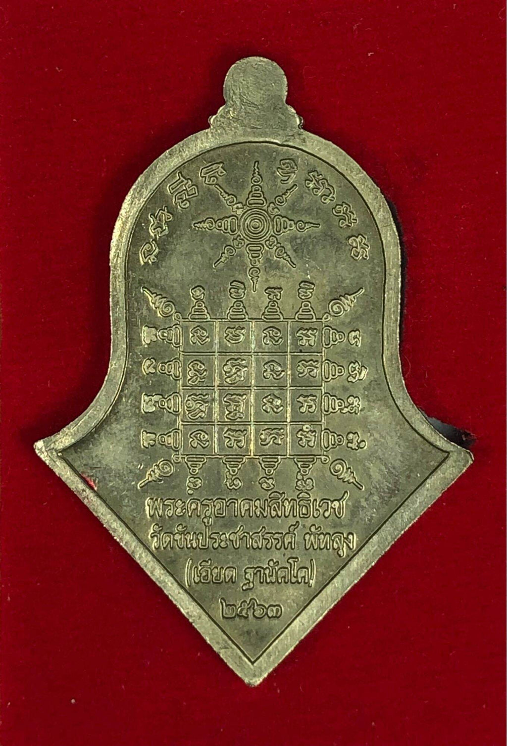Gold shield shaped Thao Wessuwan Amulet pendant with engraved yantra grid and Thai script on red background