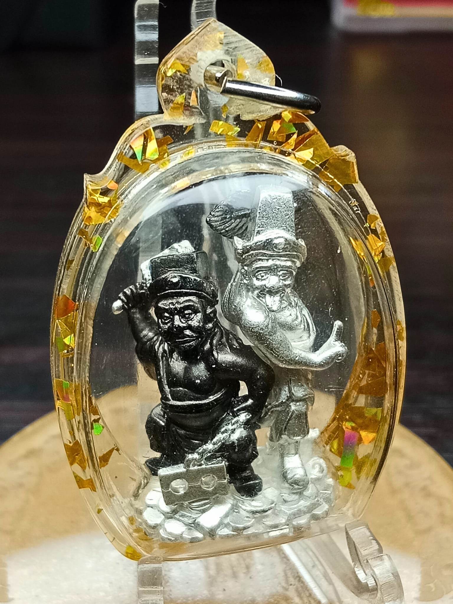 Clear casing charm with two silver deity figurines on coins and golden foil trim Tua Pae-Yee Pae Amulet - 2 Deities of Wealth.