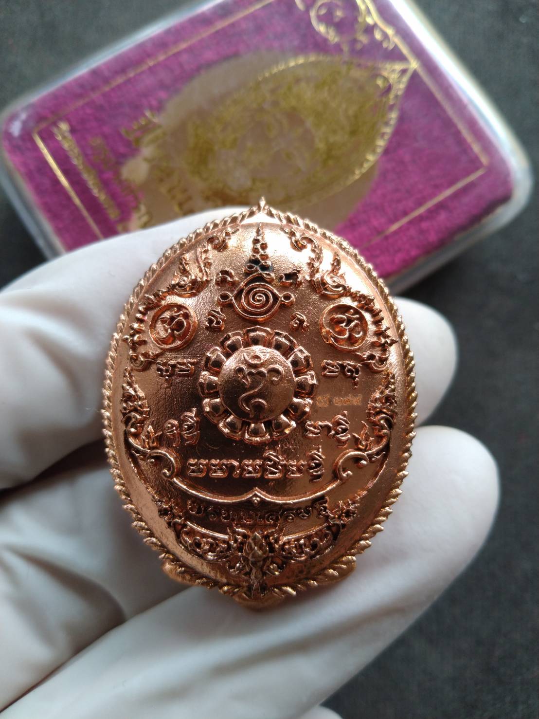 Wat Thammachai Mongkhon Brahma talisman copper oval pendant with embossed sacred symbols held in white glove