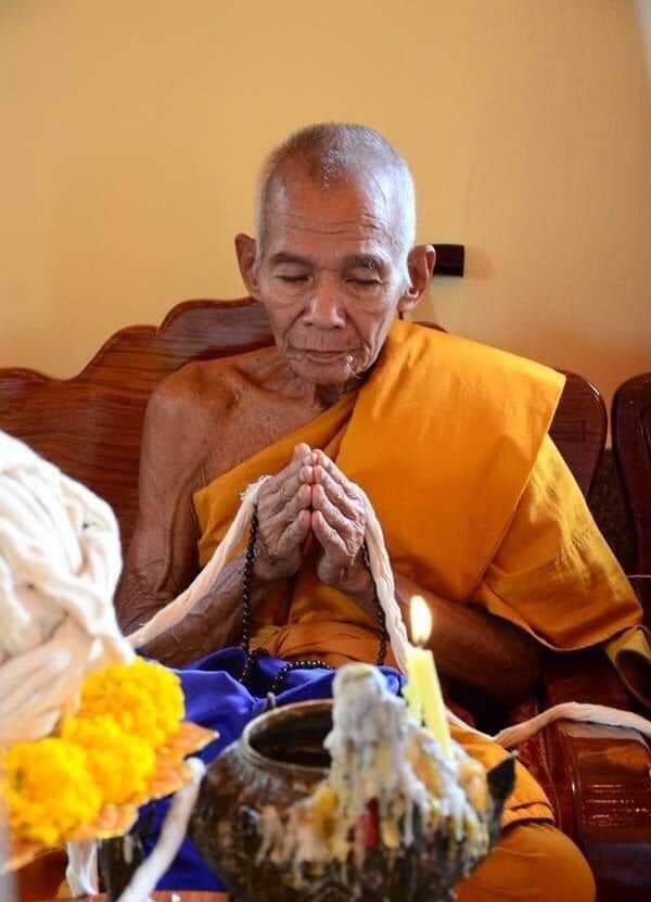 Elderly Thai monk in saffron robe praying over an authentic Thai Hanuman amulet and devotional offerings
