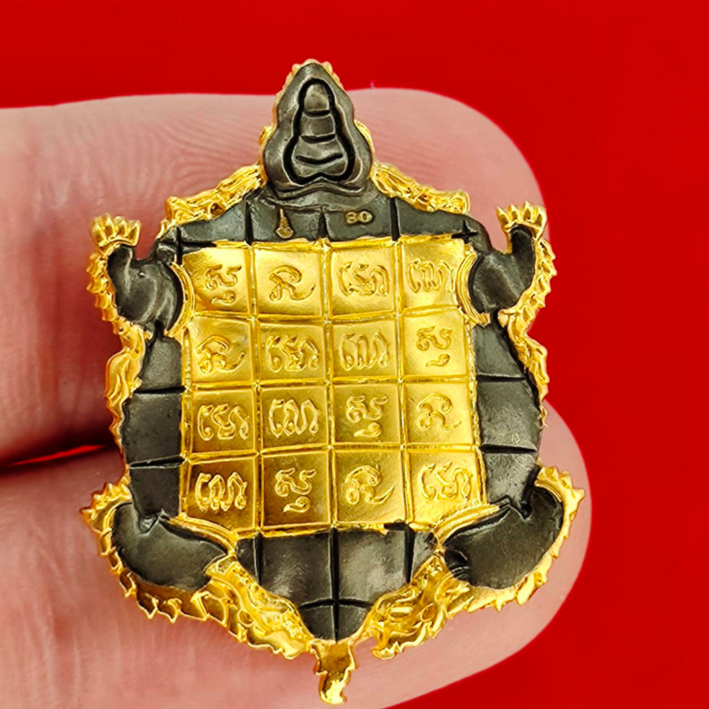 Kassapo Turtle wealth amulet gold and dark metal Thai turtle amulet with engraved yantra grid held between fingers