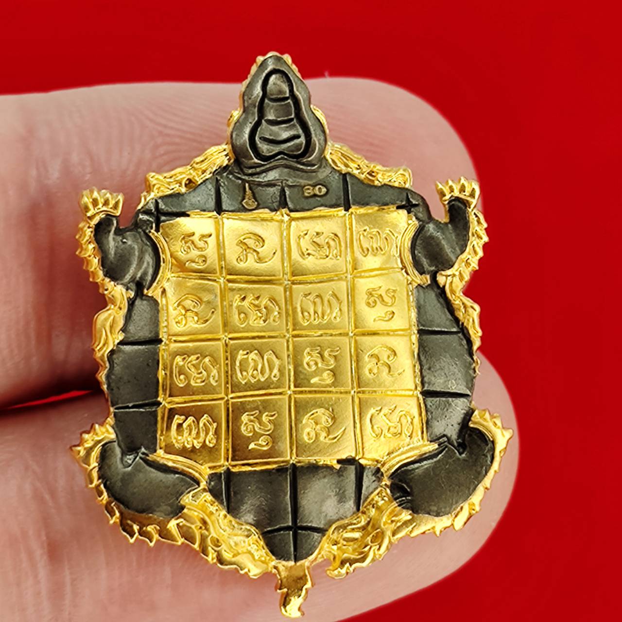 Kassapo Turtle wealth amulet gold and dark metal Thai turtle amulet with engraved yantra grid held between fingers