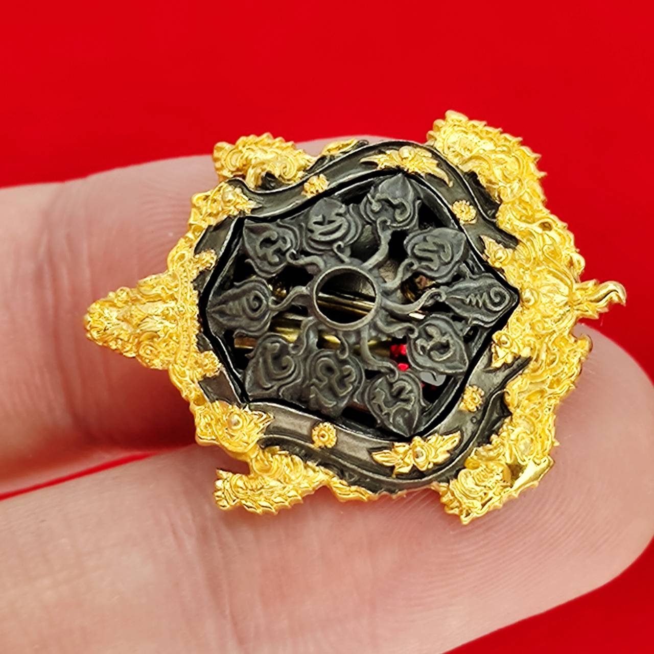 Kassapo Turtle wealth amulet gold and black ornate turtle amulet held between fingers on red background