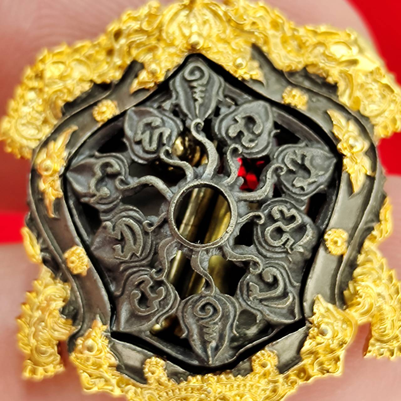 Close up of Kassapo Turtle wealth amulet showing dark carved wheel motif with center hole and gold filigree border