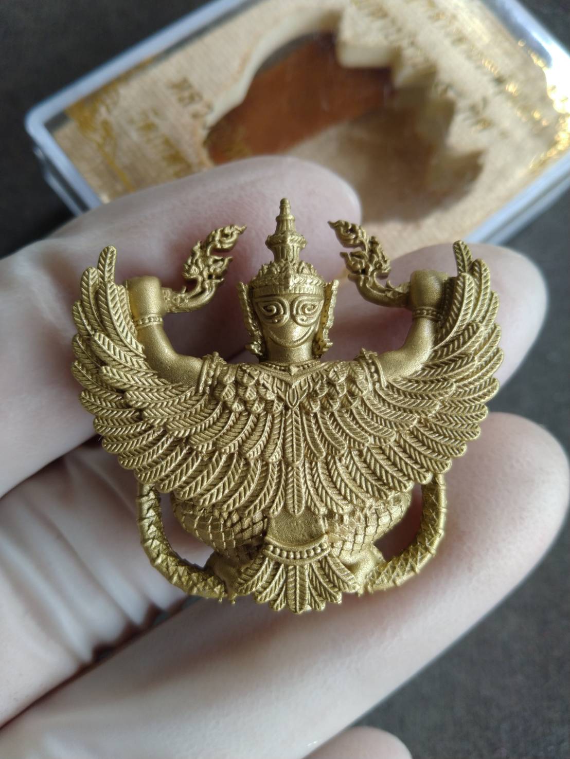 Gold Phaya Krut Garuda Amulet pendant with intricate feathered wings and Thai blessing detail held in hand
