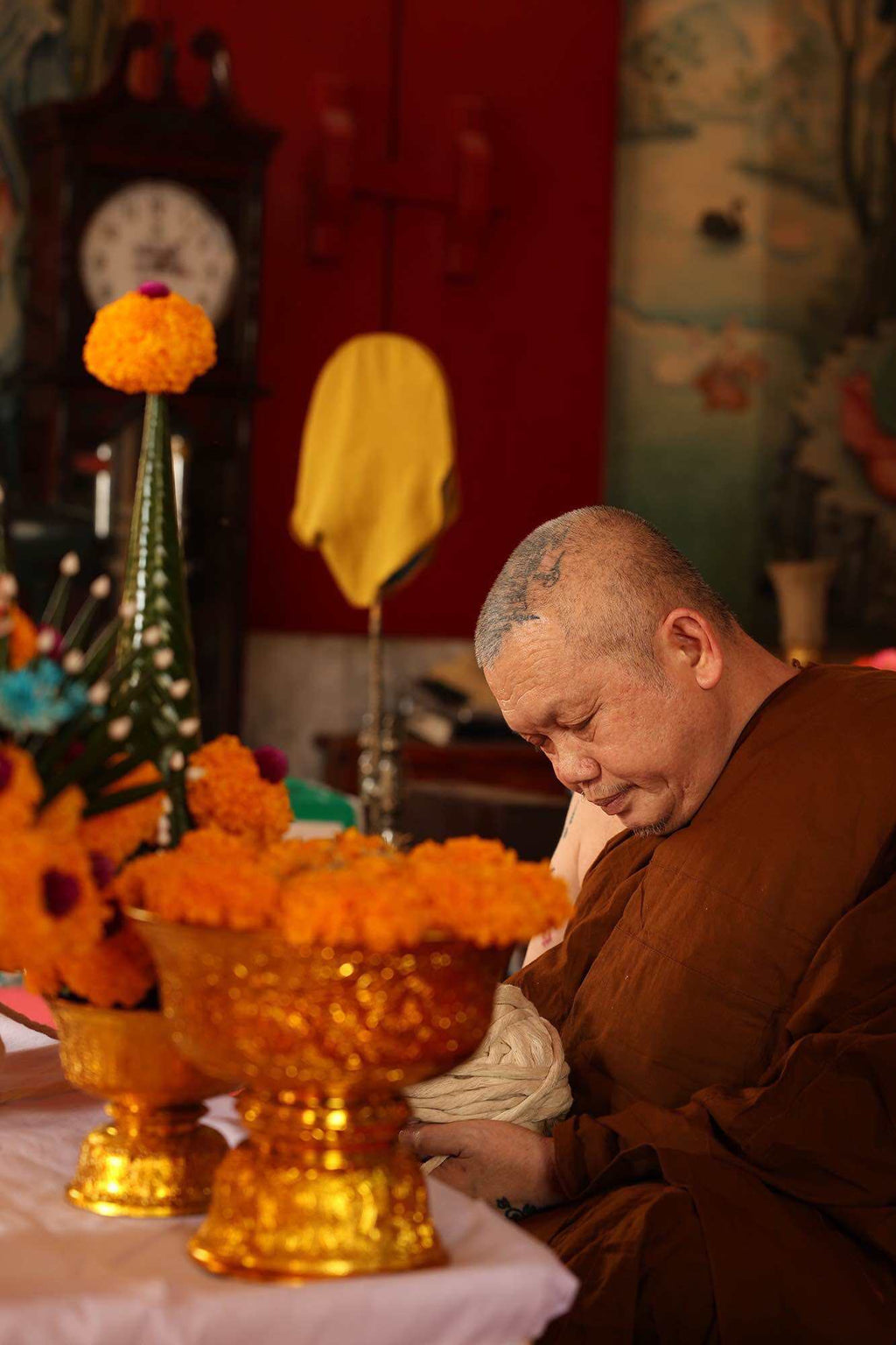 Thai Garuda car display amulet shown near a praying Buddhist monk with golden offerings and marigold flowers