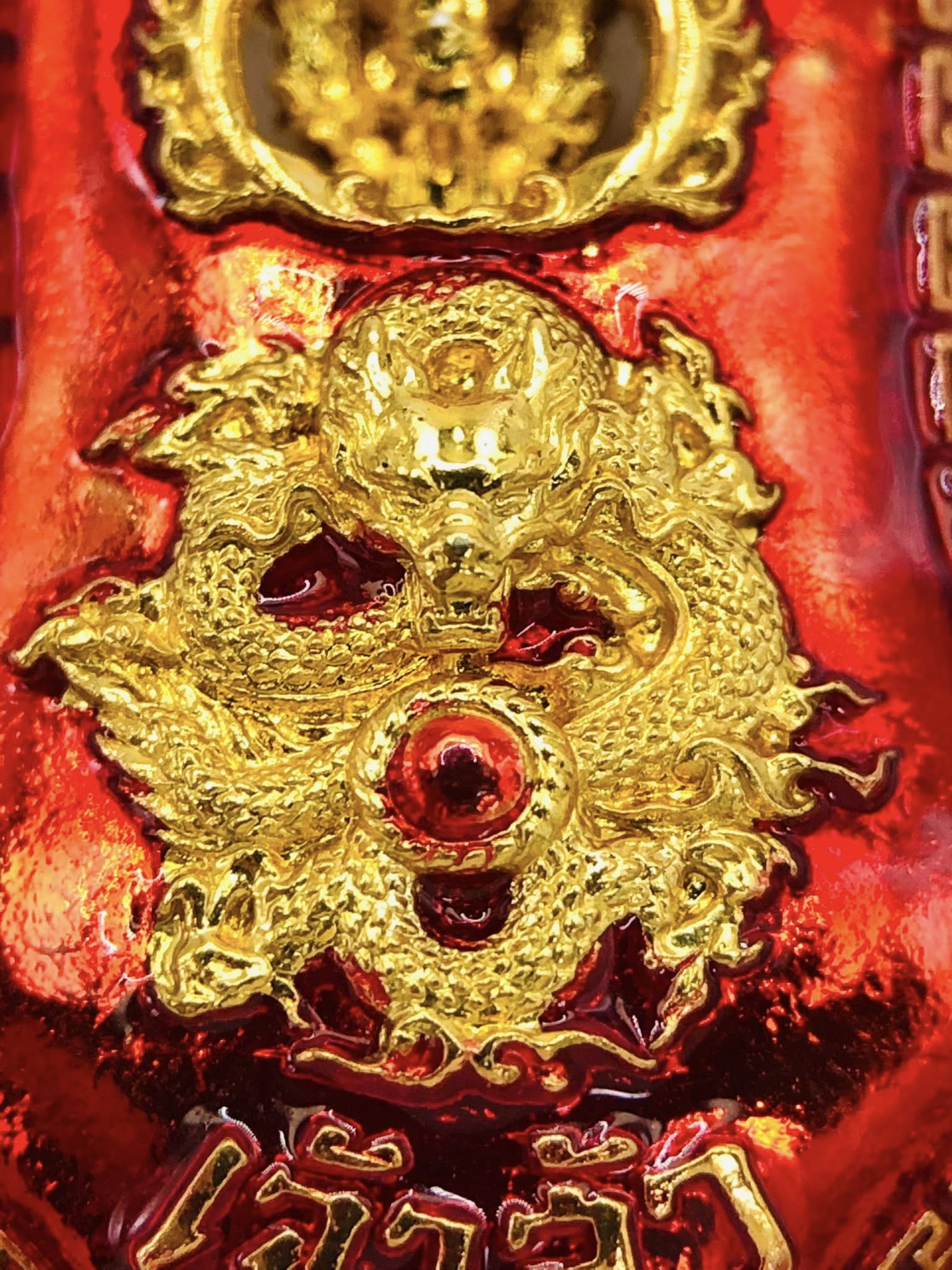 Close-up of Thao Wessuwan amulet for sale featuring intricate gold dragon design on a vibrant red background