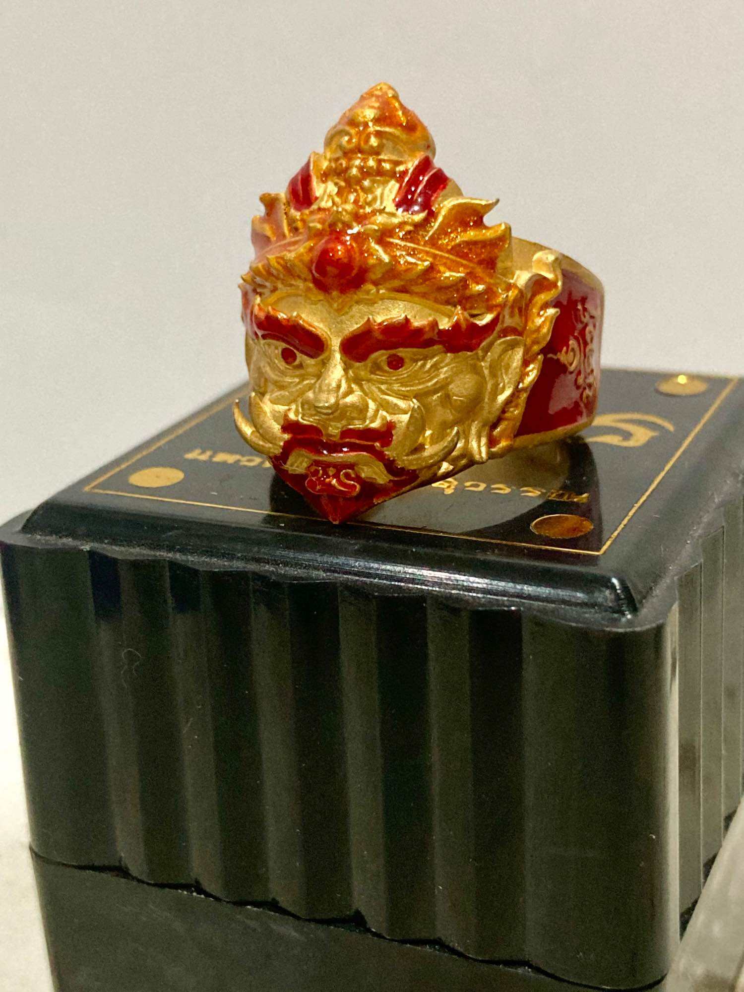 Thao Wessuwan protection ring featuring a detailed golden deity face design on a red band