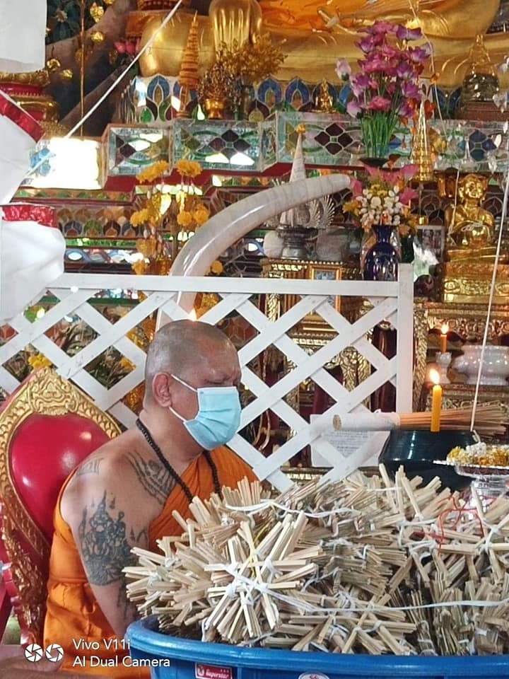 Monk at temple with Thao Wessuwan yantra cloth and offerings in a serene environment