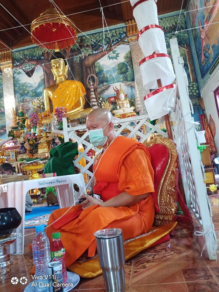 Monk sitting in a temple with Thao Wessuwan yantra cloth displayed in the background