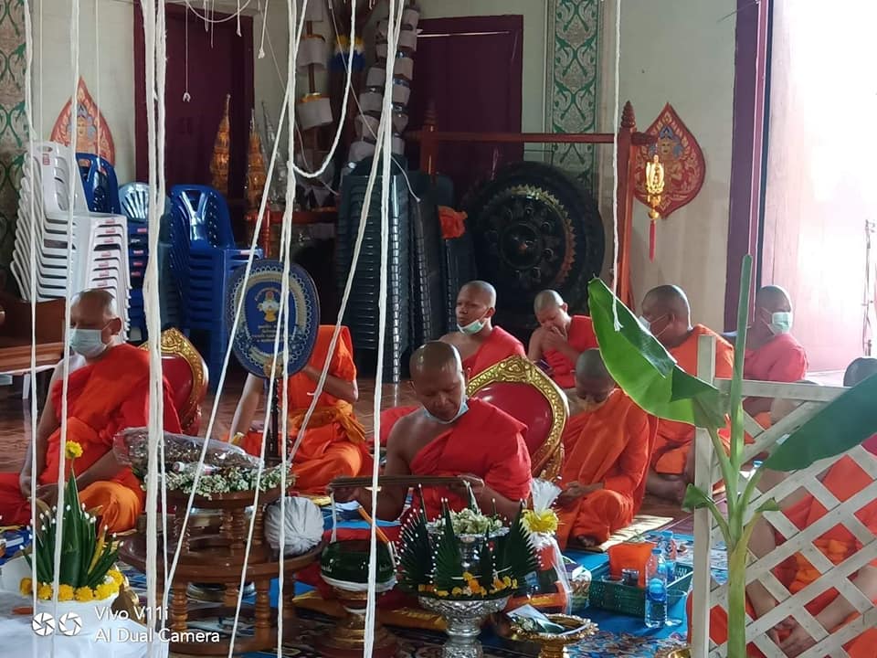 Buddhist monks in orange robes participating in a ceremony with Thao Wessuwan yantra cloth displayed
