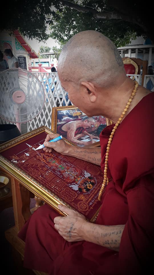 Buddhist monk creating Thao Wessuwan yantra cloth surrounded by sacred art and a fan