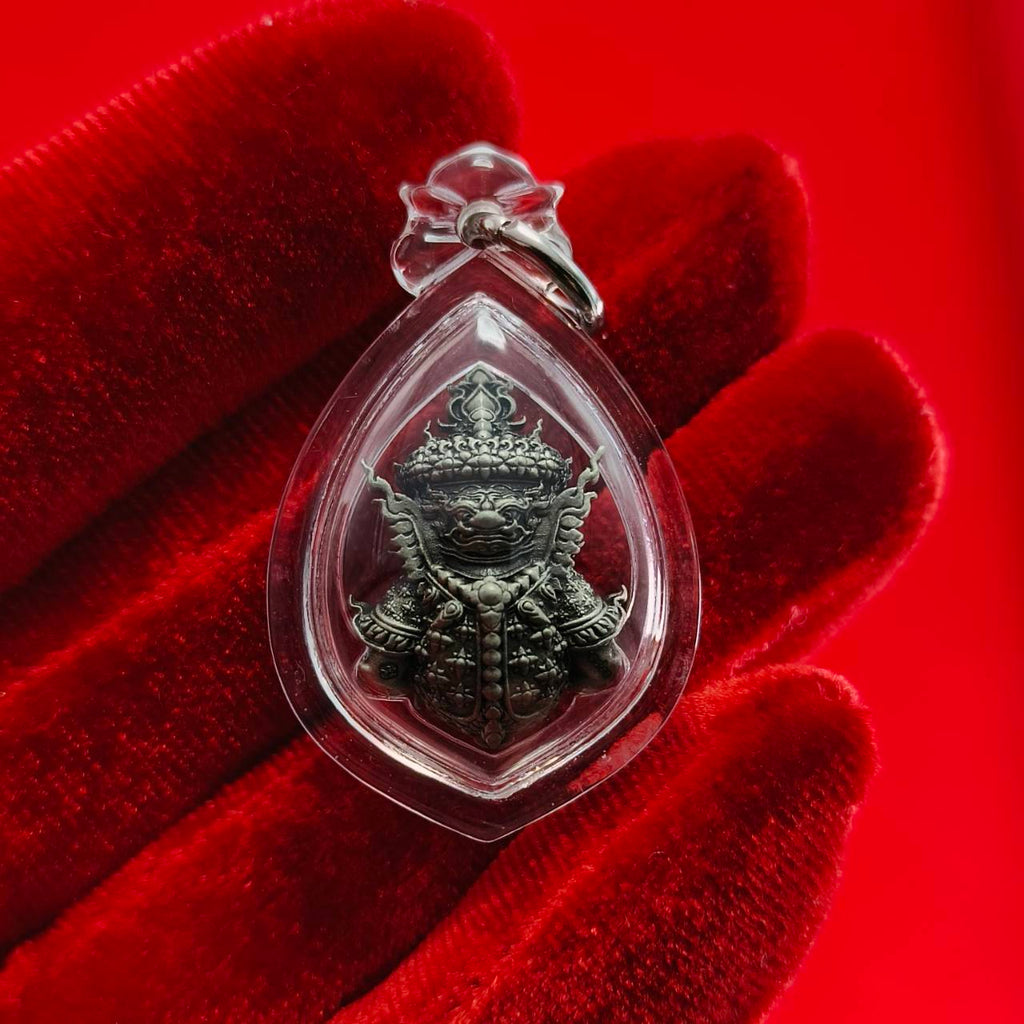 Thao Wessuwanno amulet in a teardrop casing held between fingers against a red background