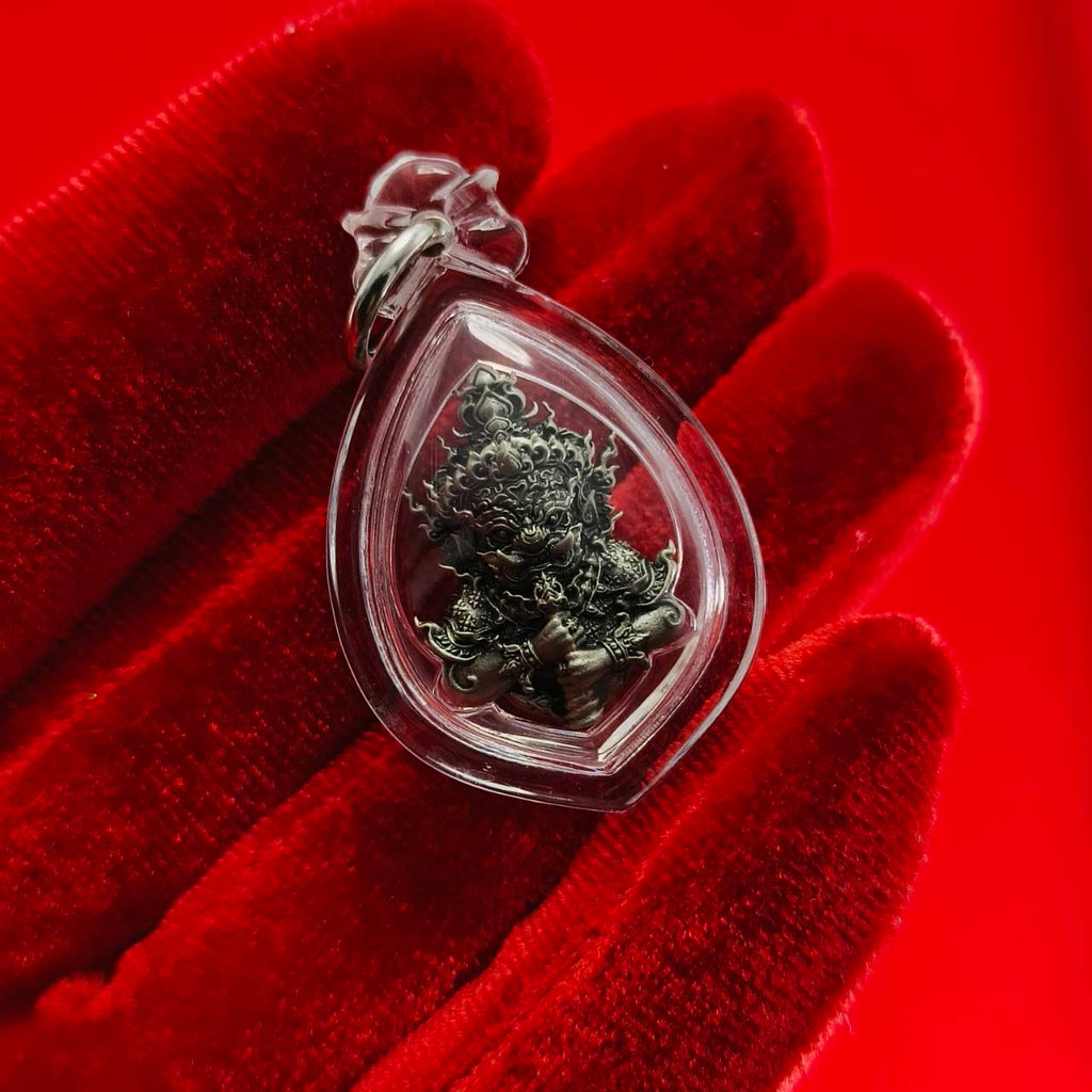 Thao Wessuwanno amulet in a clear protective casing, held on a red backdrop for decoration and spiritual belief.