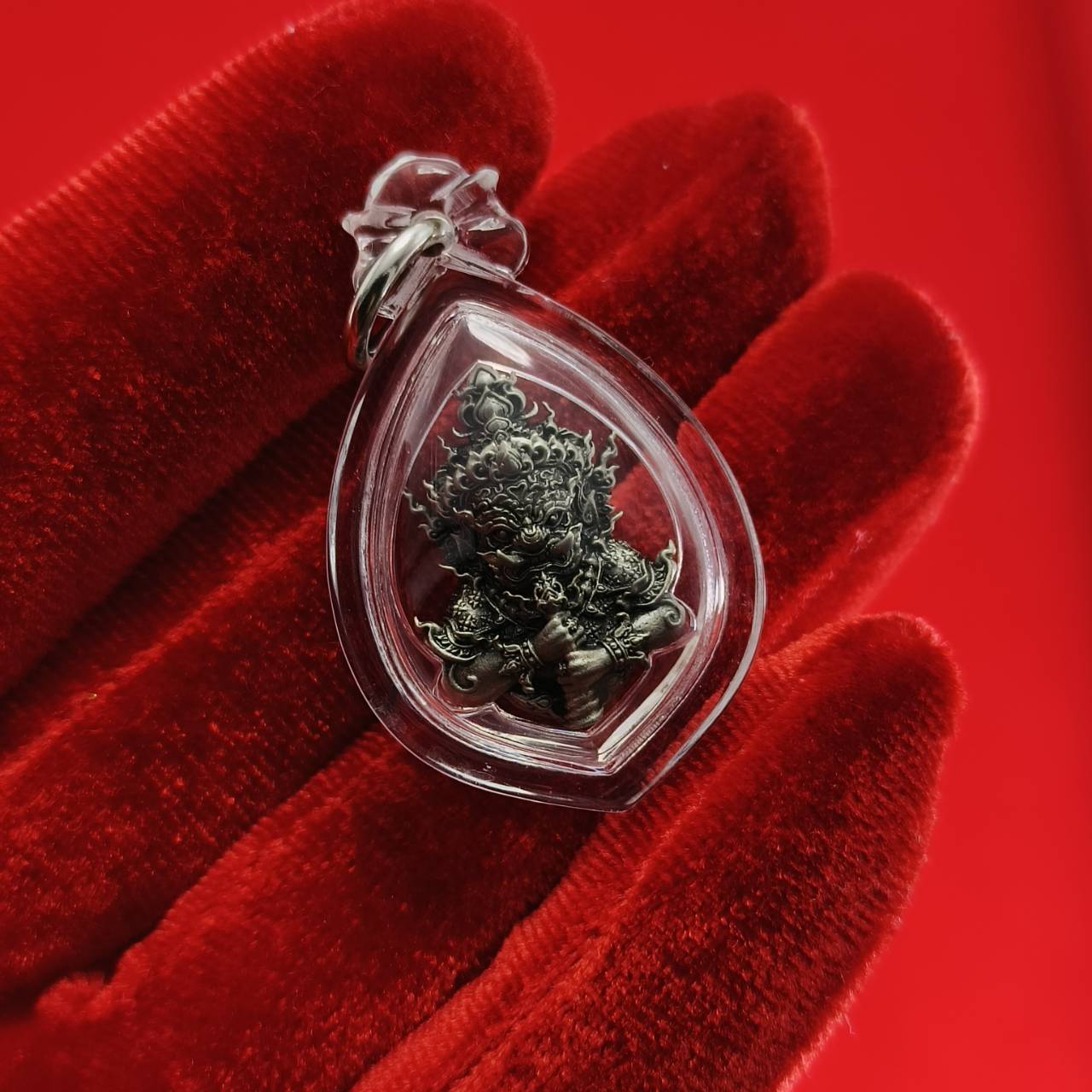 Thao Wessuwanno amulet in a clear protective casing, held on a red backdrop for decoration and spiritual belief.