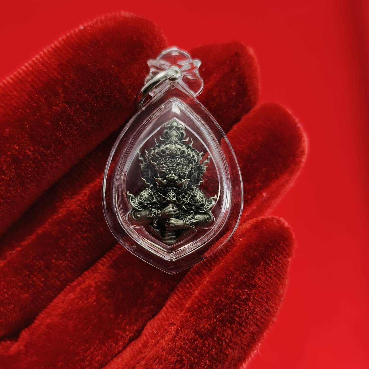 Thao Wessuwanno amulet encased in clear plastic, showcasing intricate details on a red background