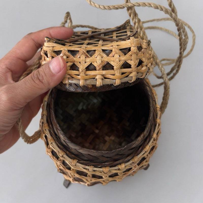 Hand holding an open traditional Thai storage box made of woven natural materials with a lid and rope handle