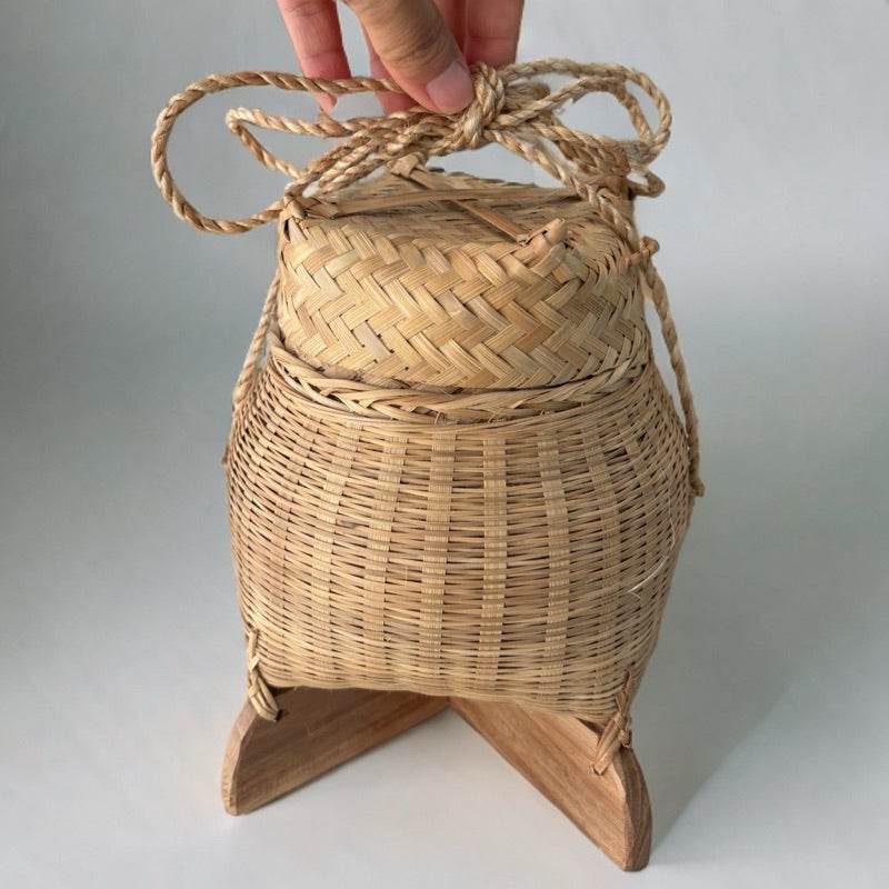 Hand holding a traditional Thai storage box made from woven natural fibers with wooden base