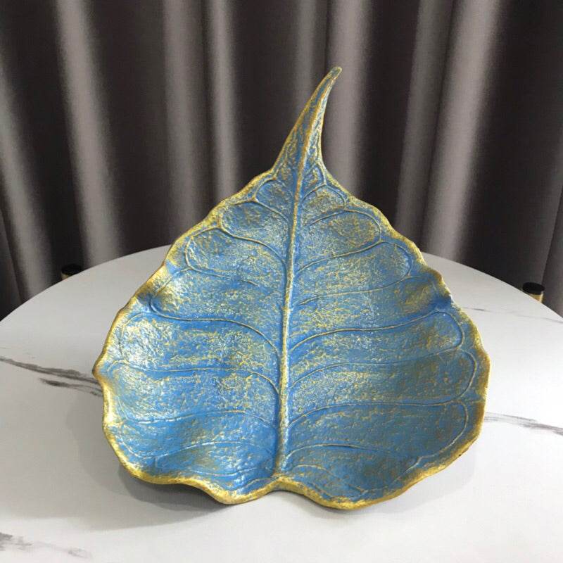 Blue and gold leaf-shaped handmade wood powder bowl on a white marble table