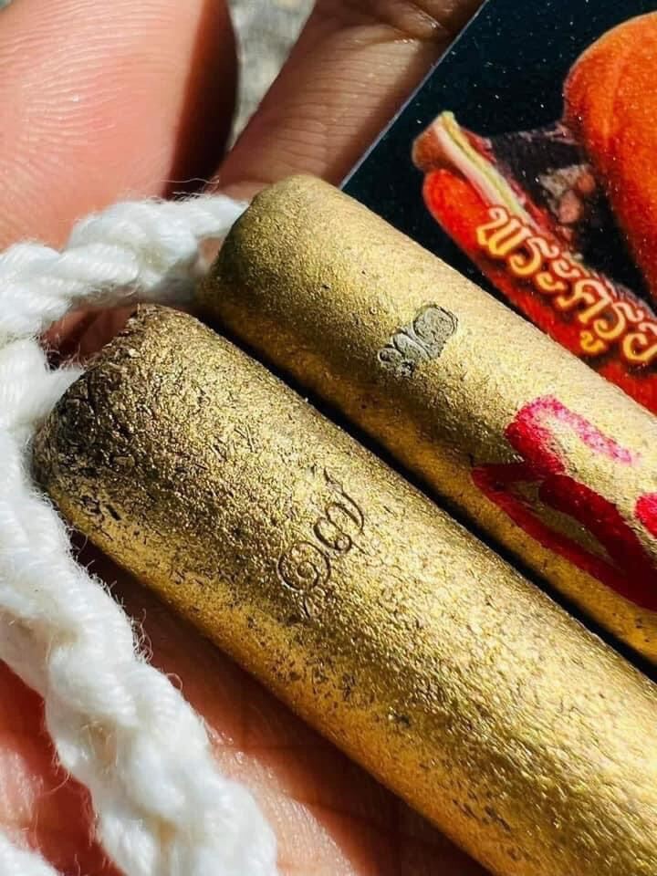 Close up of two gold takrut tubes on white cord held in hand with photo card authentic Thai spiritual talisman by Thai Blessing Co