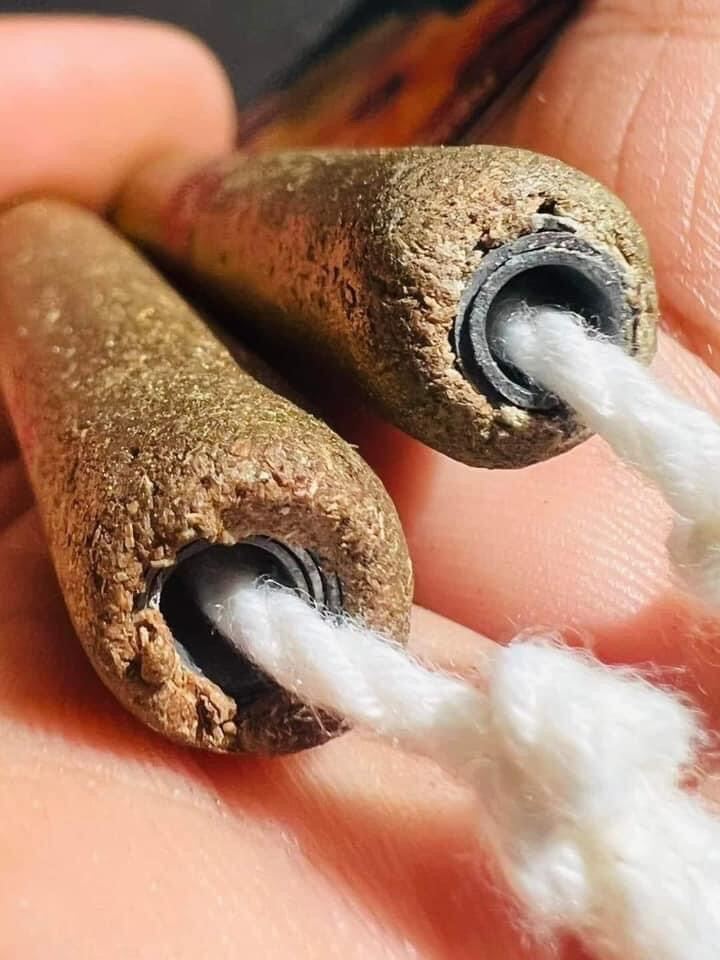 Close up of two brown cylinder amulets with cord and black eyelets authentic Thai spiritual talisman for wearing