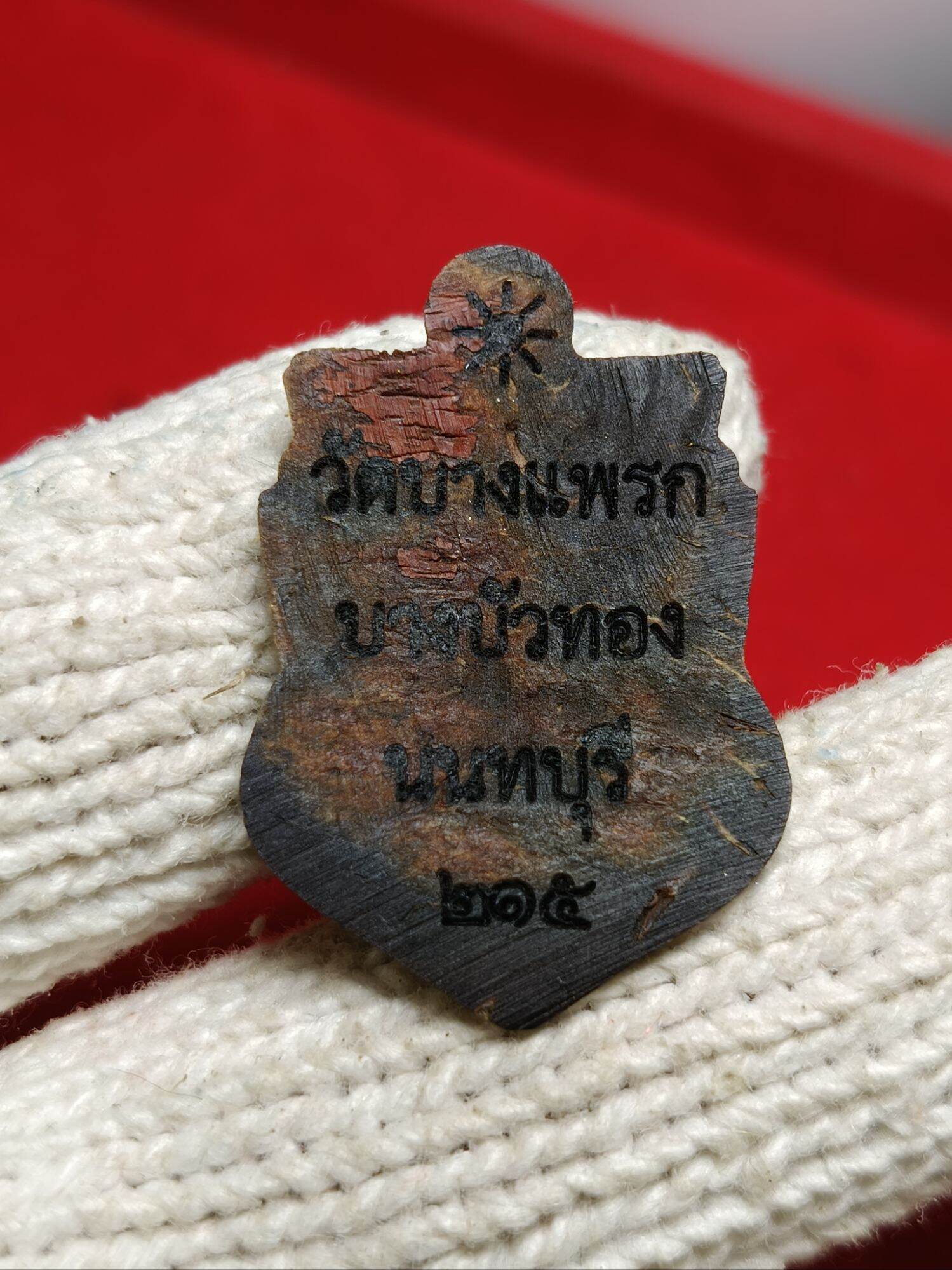 one-eyed Rahu Thai amulet metal shield pendant showing aged back with Thai inscriptions held in white glove