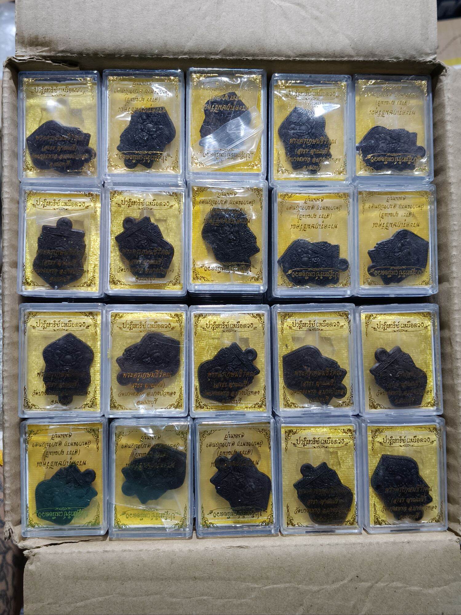 Box of 20 one-eyed Rahu Thai amulet pendants in clear plastic cases with gold backing by Thai Blessing Co