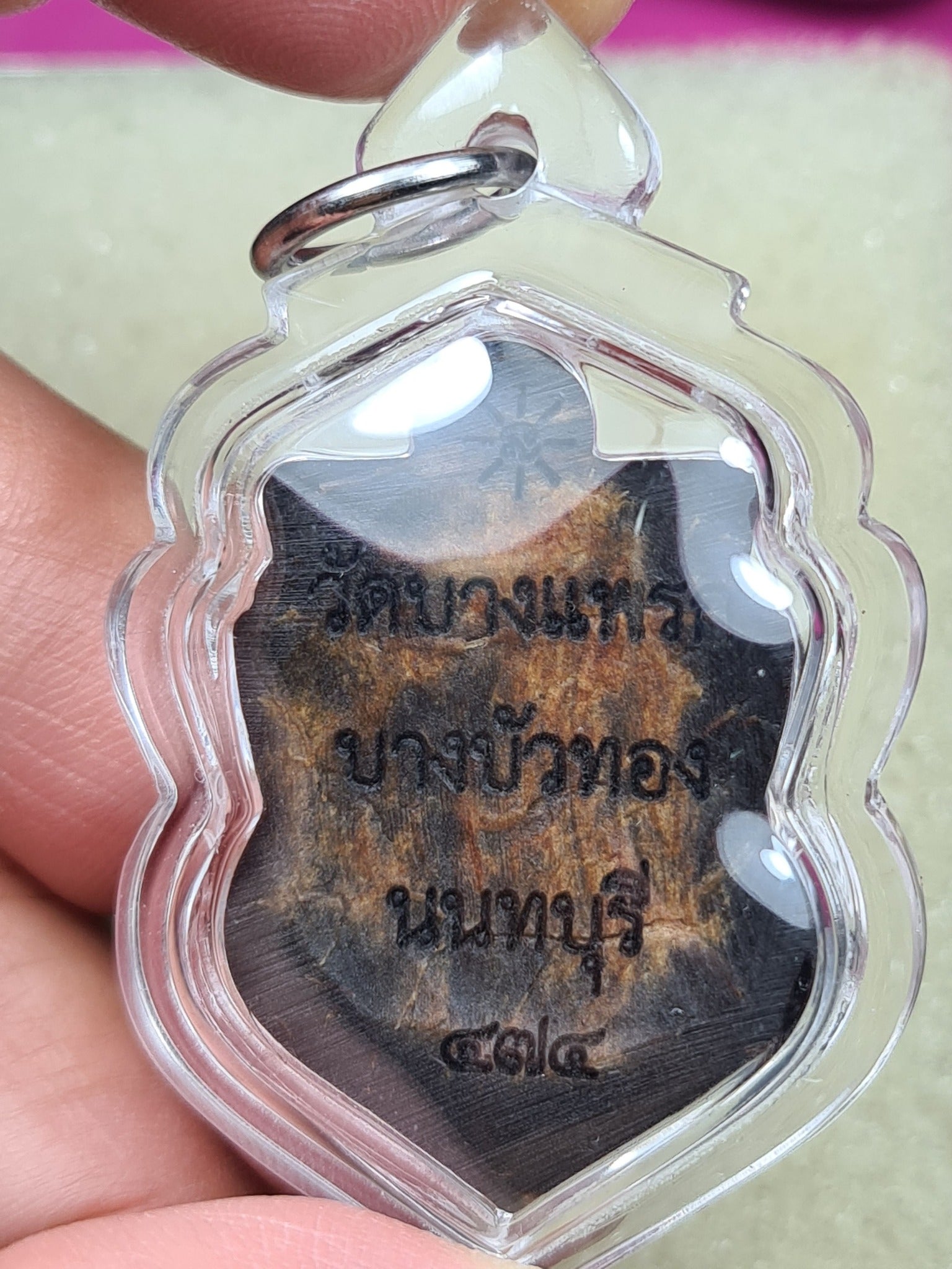 one-eyed Rahu Thai amulet wooden pendant with Thai script in clear plastic case held by hand by Thai Blessing Co