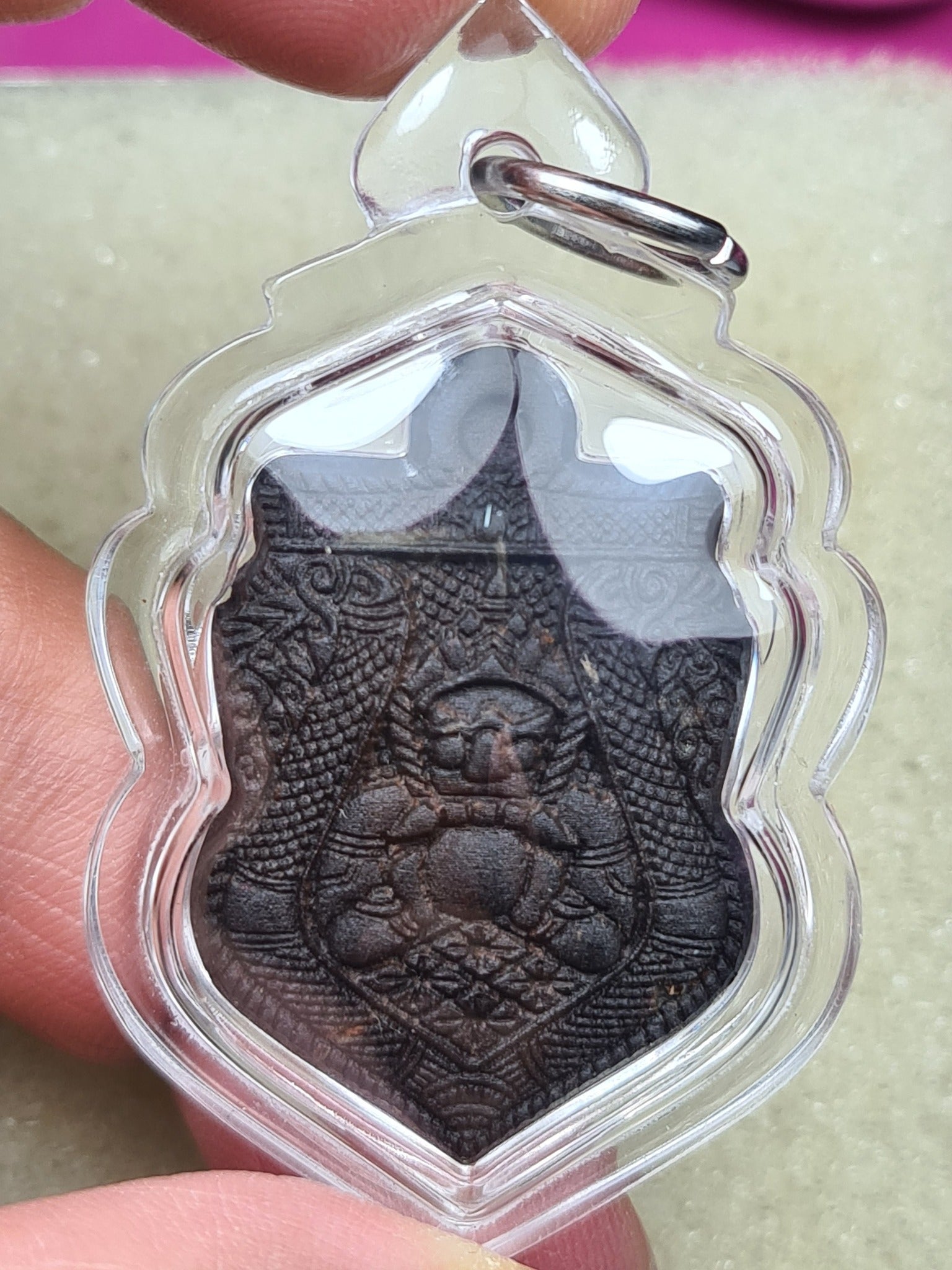 one-eyed Rahu Thai amulet pendant in clear plastic case held by fingers with carved dark talisman details