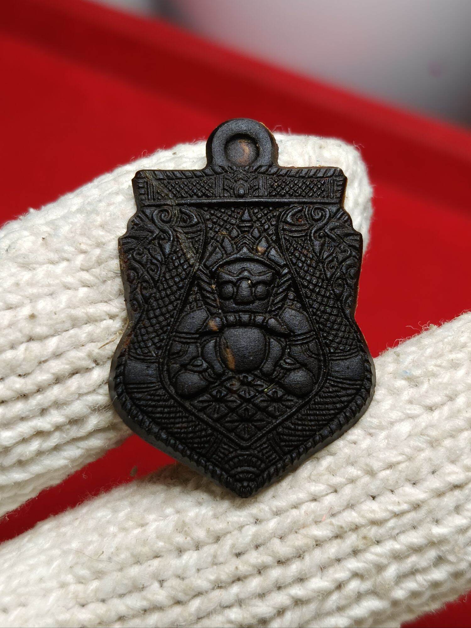 Dark carved metal shield pendant one-eyed Rahu Thai amulet held in white knit glove by Thai Blessing Co