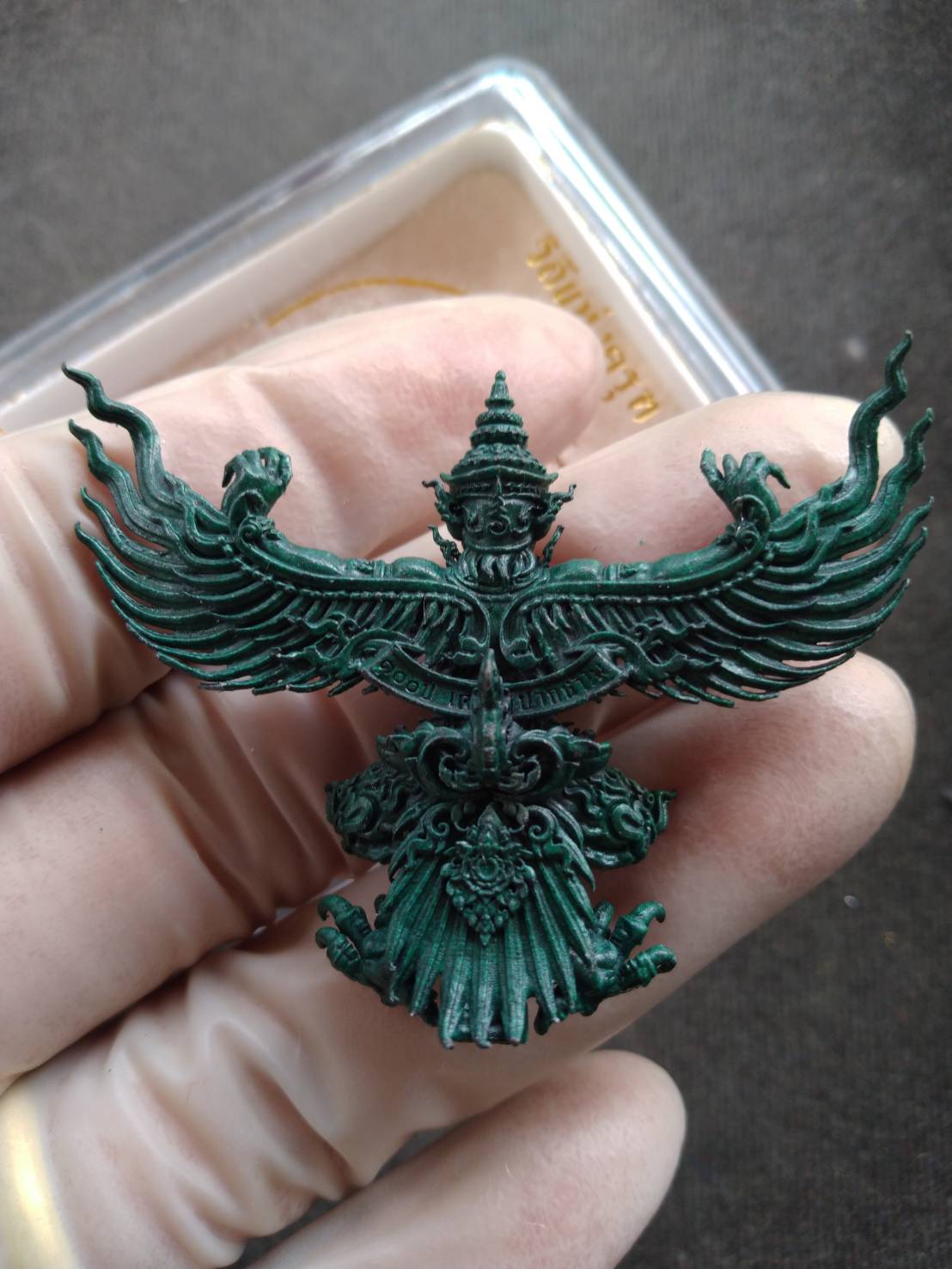 Hand holding green patina Phaya Krut amulet blessed by Luang Phor Phat. Ornate Garuda pendant talisman