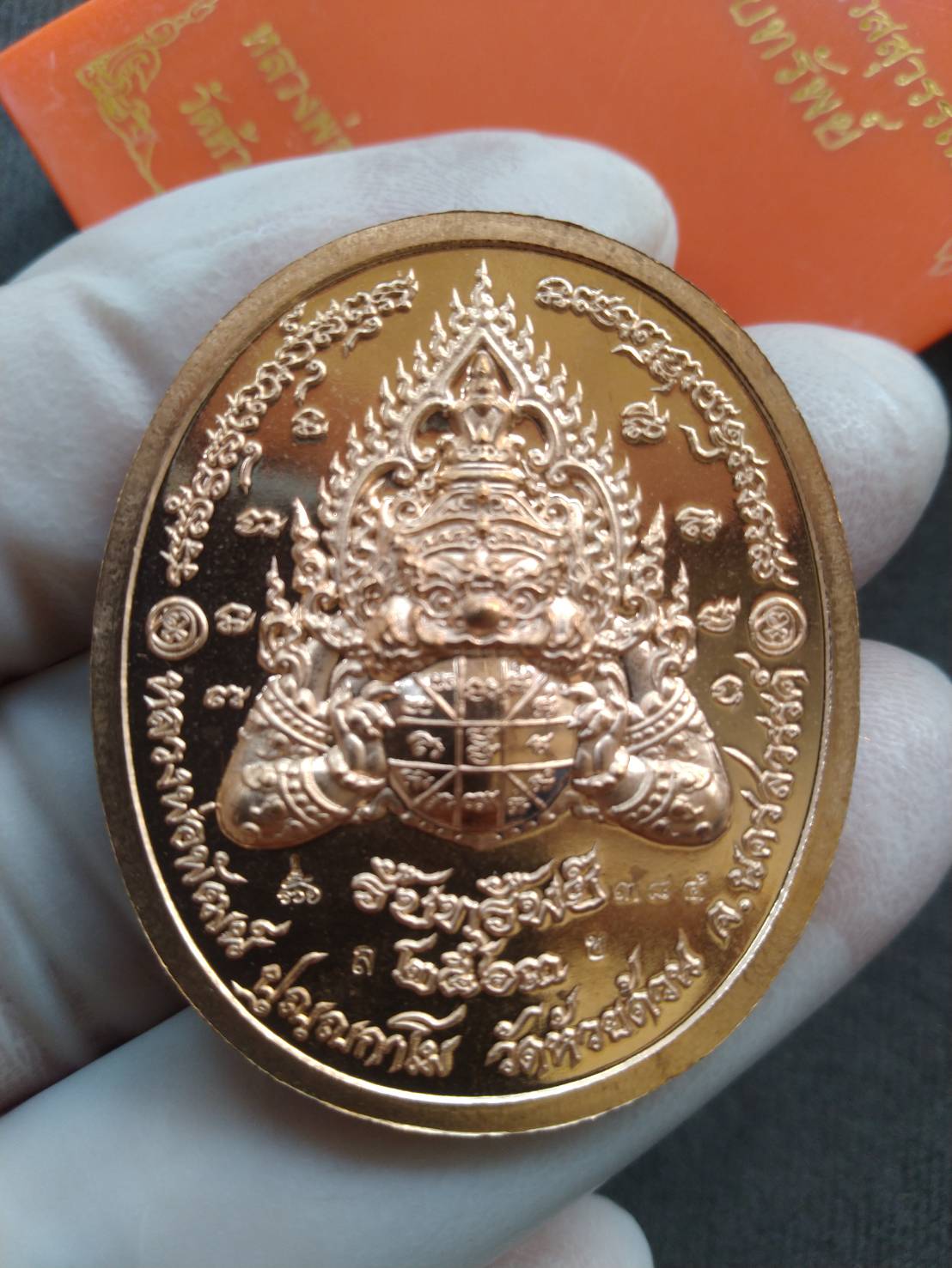Gold oval Thao Wessuwan amulet for protection medallion with Thai inscriptions held by gloved hand