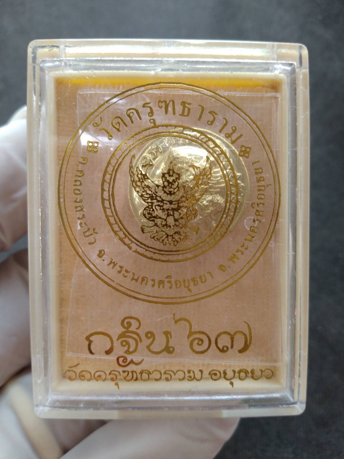 Garuda protection medallion in clear plastic display case gold medallion with Thai temple seal held by gloved hand