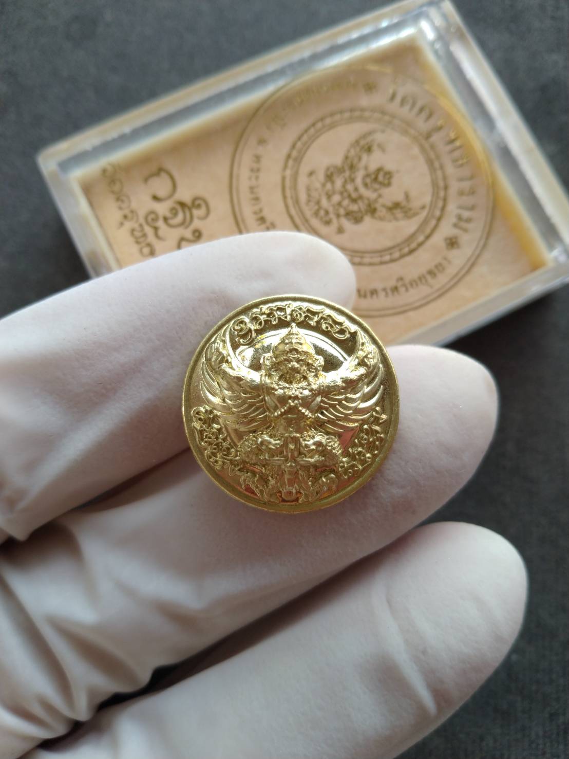 Gold Garuda protection medallion held in white gloved hand with Thai Blessing Co box packaging