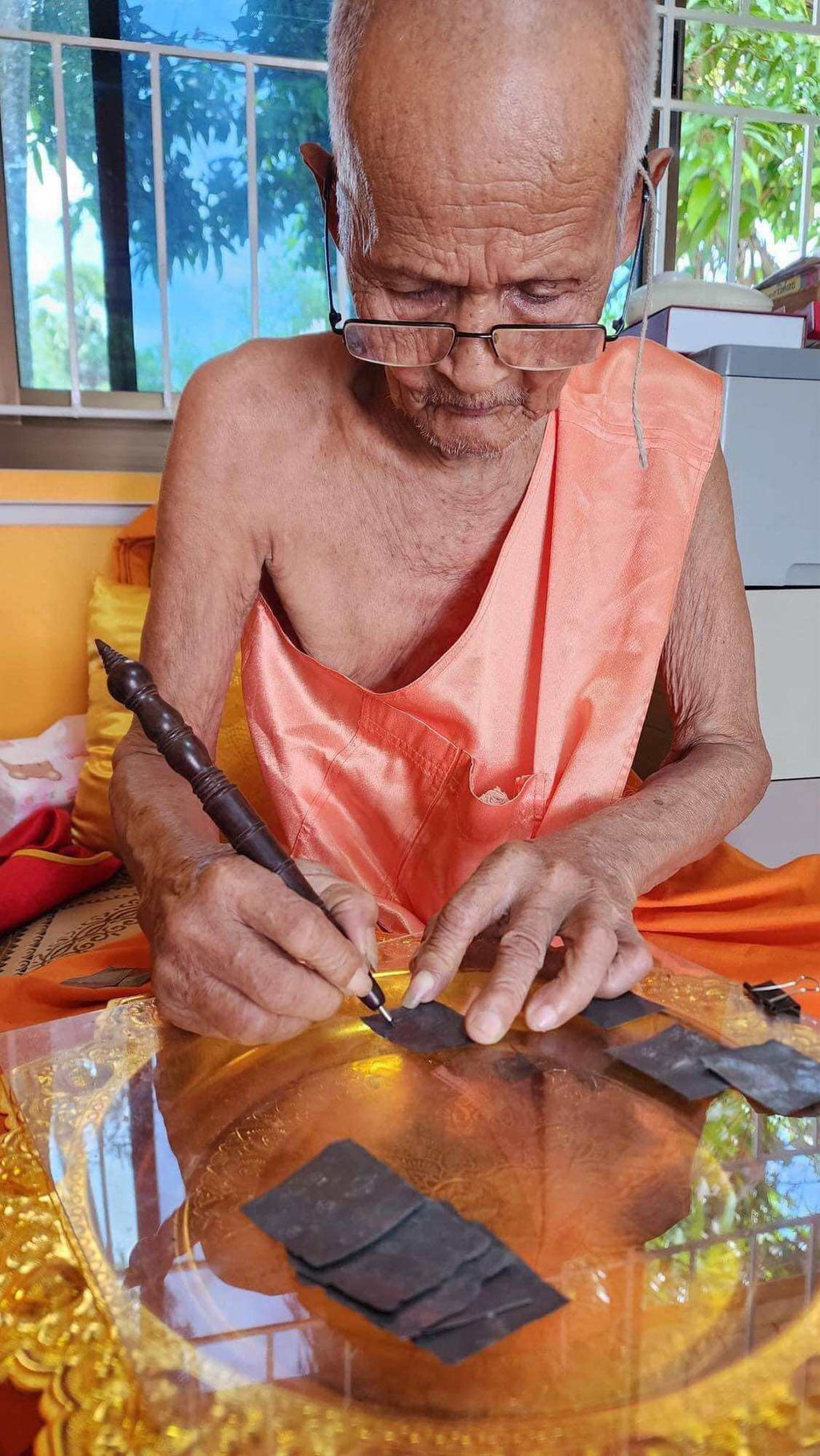 Elderly Thai monk hand engraving Mongkol Hemarat Kring spiritual charm on brass plate during blessing ritual
