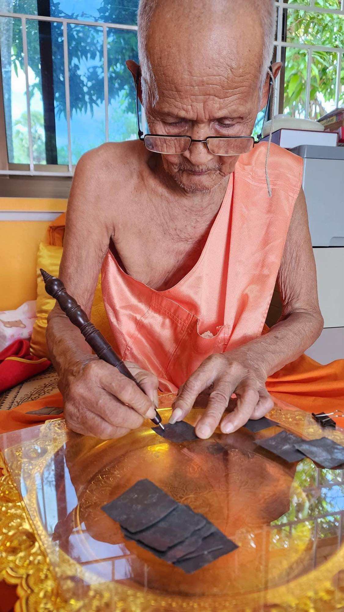 Elderly Thai monk hand engraving Mongkol Hemarat Kring spiritual charm on brass plate during blessing ritual