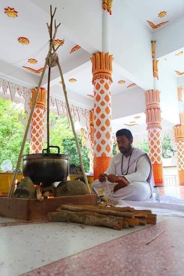 Monk crafting sacred black sticky rice bead amulet during blessing ritual in Thai temple