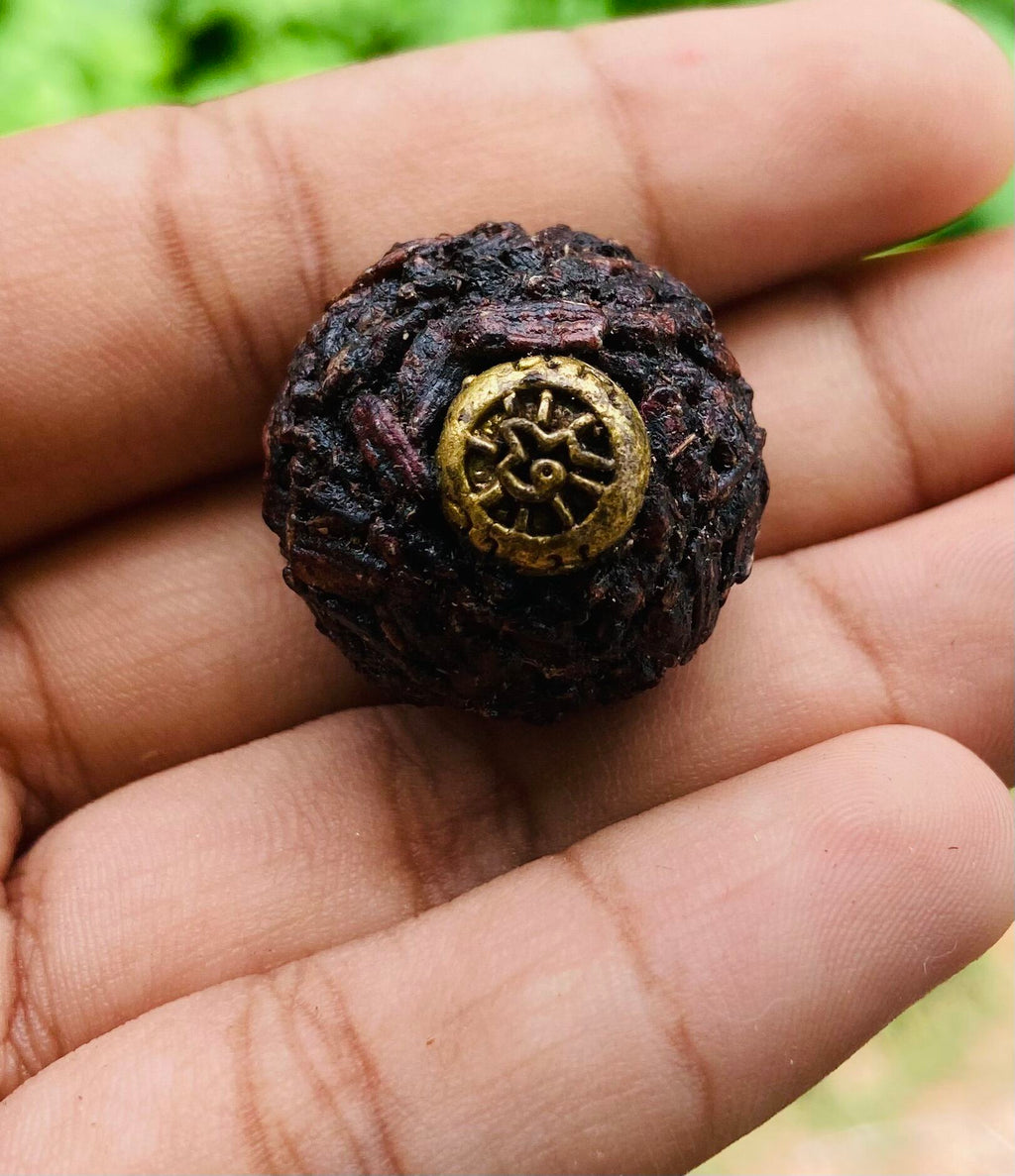 Hand holding Thai Blessing Co sacred black sticky rice bead amulet with woven rice texture and brass wheel charm