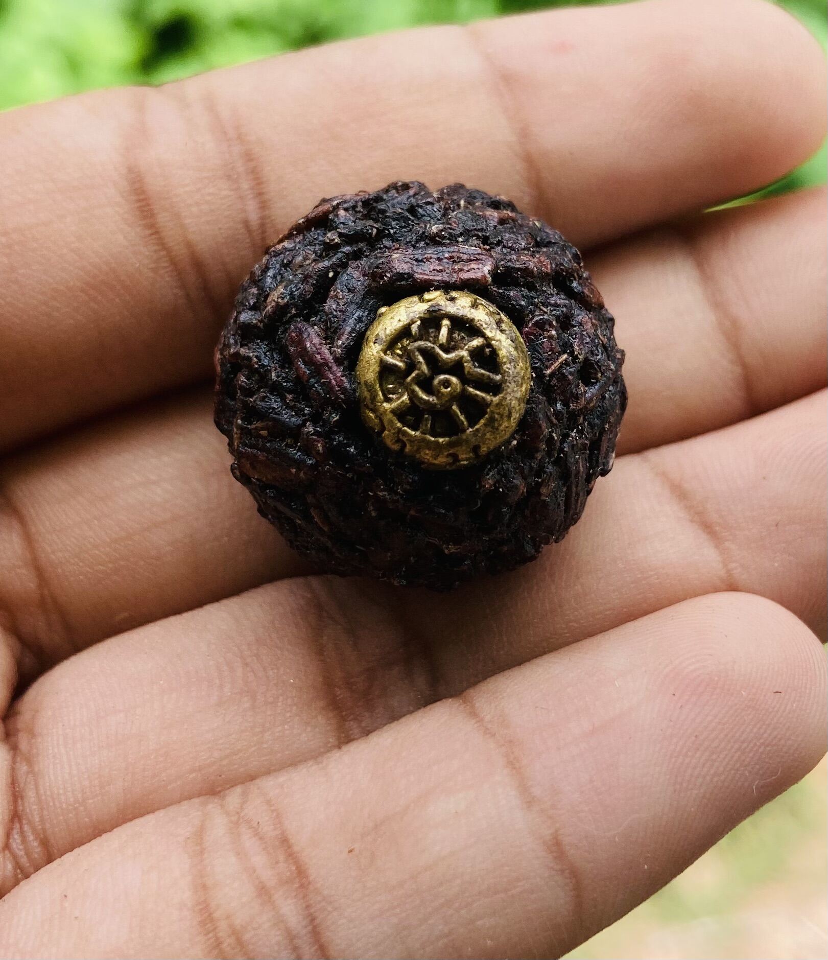Hand holding Thai Blessing Co sacred black sticky rice bead amulet with woven rice texture and brass wheel charm