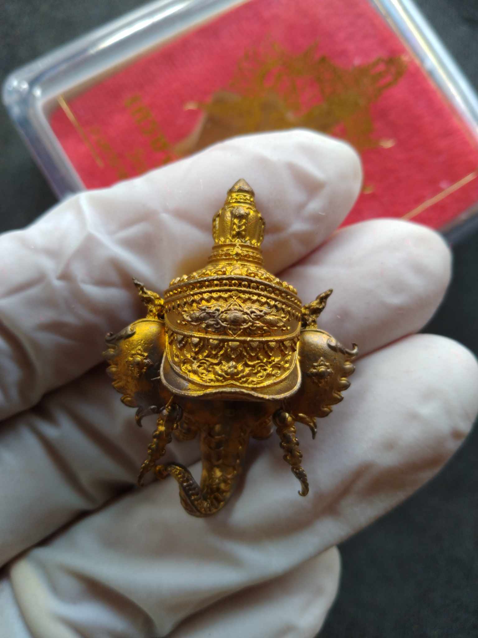 Handheld gold Miracle of Wealth Ganesha amulet with ornate crown and intricate carving held in glove