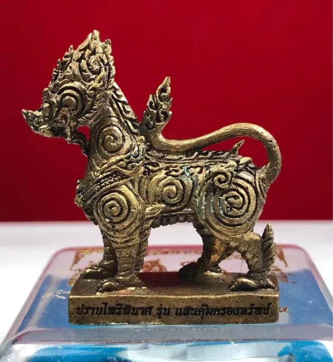 Ornate gold metal Singha Guardian Amulet figurine with spiral patterns on display base and red background